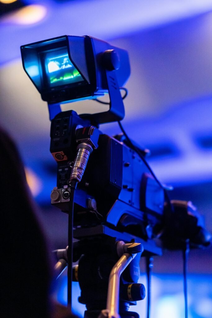 Close-up of professional video camera capturing a scene at an indoor event with ambient blue lighting.